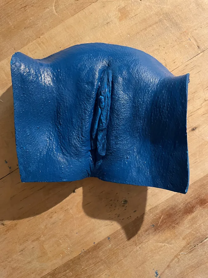 Vulva cast in deep blue pigmented resin on a wooden table