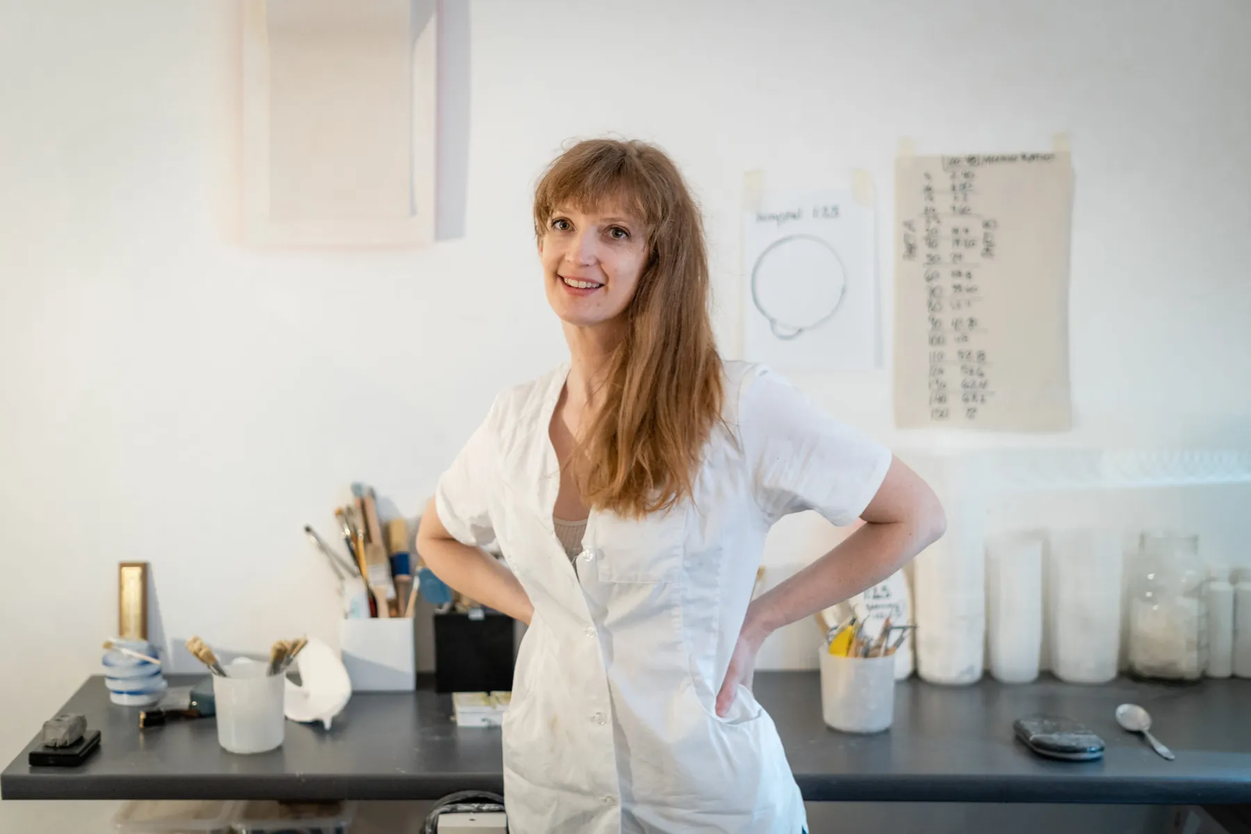Brooke Meenan smiling in her studio in a white work coat