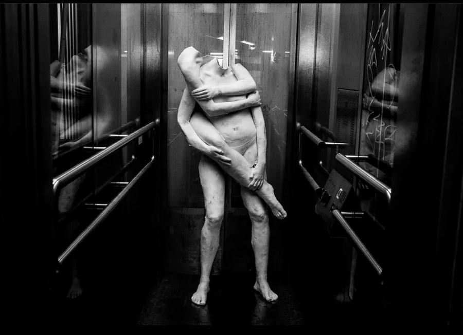 Full-body plaster sculpture of two entwined figures standing in a lift